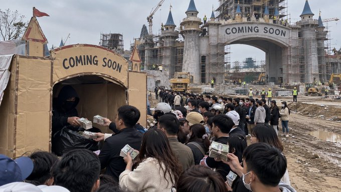 A large crowd of people gathers at a construction site of a theme park, with people exchanging cash bundles at a 'COMING SOON' booth and a castle archway in the distance.