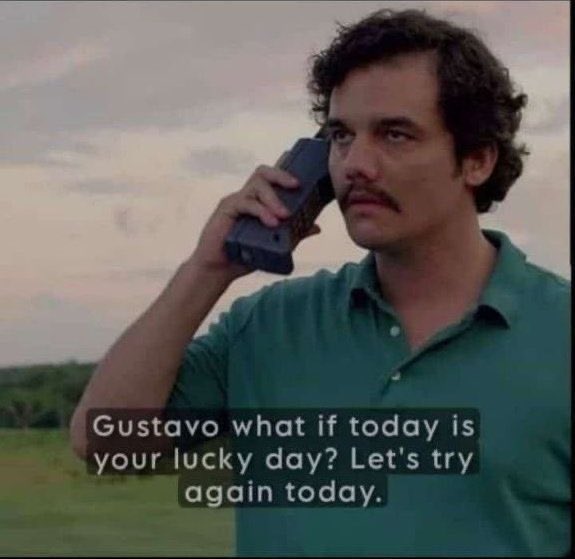 A man with a mustache in a green polo shirt holds a large early mobile phone to his ear, with subtitles reading 'Gustavo what if today is your lucky day? Let's try again today.'