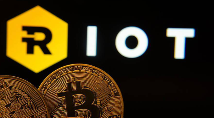 Two physical Bitcoin tokens sit in front of the illuminated Riot Platforms (RIOT) logo against a dark background, visually reinforcing the article about Riot's major Q2/2026 decision to sell 4,300 BTC to fund AI data center expansion.