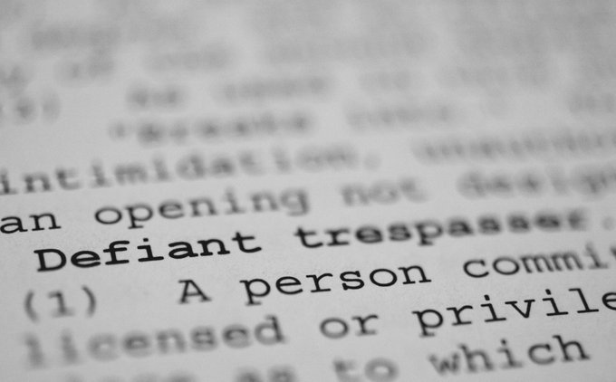 A close-up of a dictionary page focuses on the bolded word 'Defiant,' showing its definition as 'A person committing trespass.'