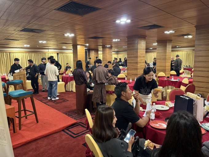 A bustling banquet hall filled with people gathered around round tables with red tablecloths, with staff in uniform and diners enjoying a meal.