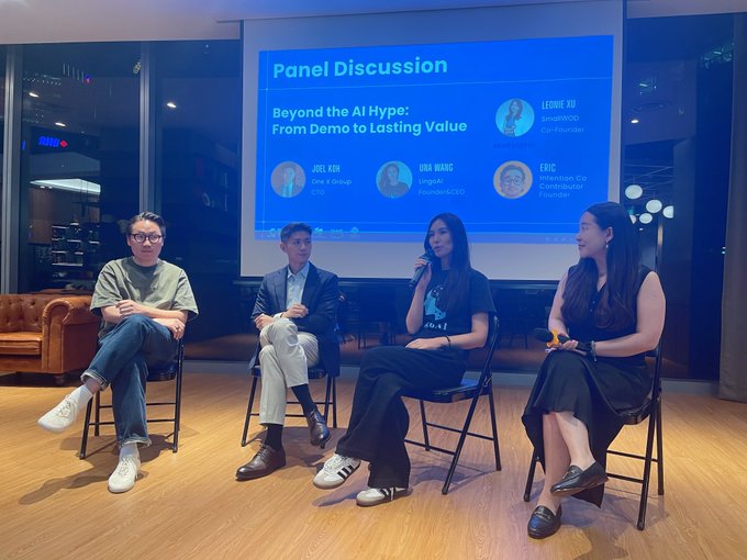 A photo of four panelists seated on stage during a presentation at the TOKEN2049 Afterparty at OGBC Innovation Hub in Singapore, with a microphone being passed among the speakers. The projection screen reads “Panel Discussion” and “Beyond the AI Hype: From Demo to Lasting Value,” listing speakers Leanne Yau (Moderator), Joel Xin, Una Wang, and Eric Feng with their affiliations.