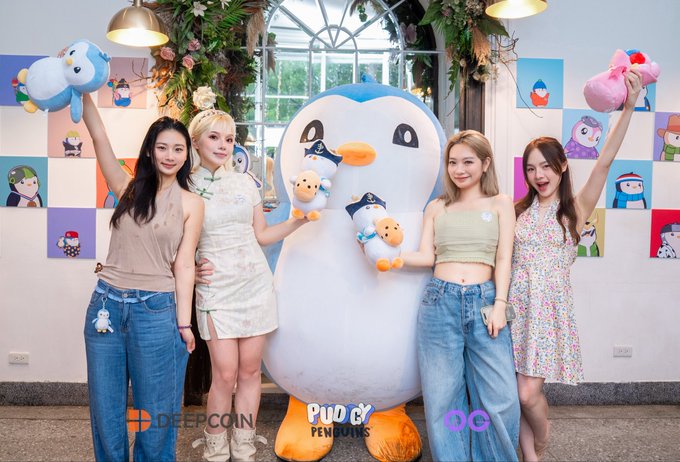 Four young women pose with plush toys alongside a large Pingu mascot at an indoor event branded with 'Pudgy Penguins' and 'DEEPCON' watermarks.
