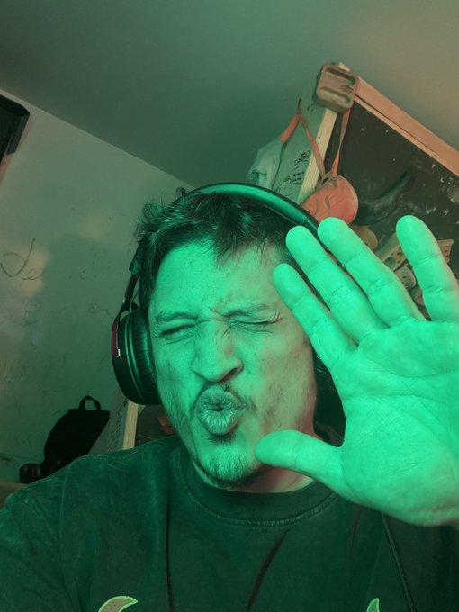 A man wearing headphones squints and pouts while holding up his hand, bathed in green lighting, humorously mirroring the "green af" market gains mentioned in the caption.