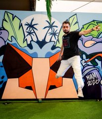 A man joyfully jumps in front of a colorful tropical-themed mural featuring palm trees and the text "Miami 2022." The image likely represents a company milestone celebration, aligning with the post's announcement about reaching major achievements like 100 million downloads, and the mention of Miami suggests the event location tied to the company's success.
