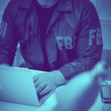 An FBI agent in a jacket marked "FBI" types on a laptop, illustrating the arrest of agent Patrick Yaroch, who allegedly stole nearly $1 million in cryptocurrency by exploiting his law enforcement access.