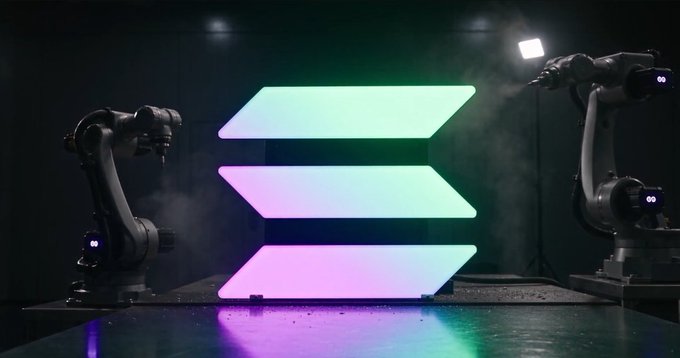 Two Unitree robots stand on either side of three glowing, gradient-lit chevron signs (in green, white/blue, and pink/purple) on a dark stage, visually representing the post's point about robots ("machines") becoming part of the onchain ecosystem alongside PEAQ, World ID, P256, and Solana.