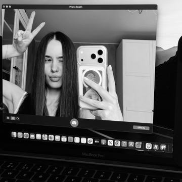 A black and white photo of a young woman taking a mirror selfie with a peace sign, displayed on a MacBook Pro Photo Booth window.