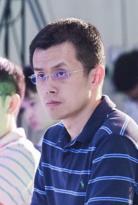A man with glasses and short black hair wearing a navy blue striped polo shirt looks off to the side with a serious expression. The image likely shows CZ (Changpeng Zhao), founder of Binance, as referenced in the anniversary post celebrating 9 years of their connection.