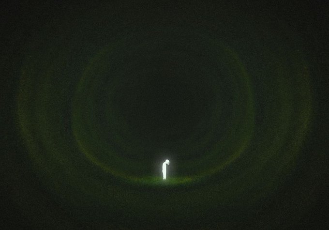 A dark, grainy image showing a bright green, glowing circular halo or ring of light surrounding a small, solitary white silhouette in the center.