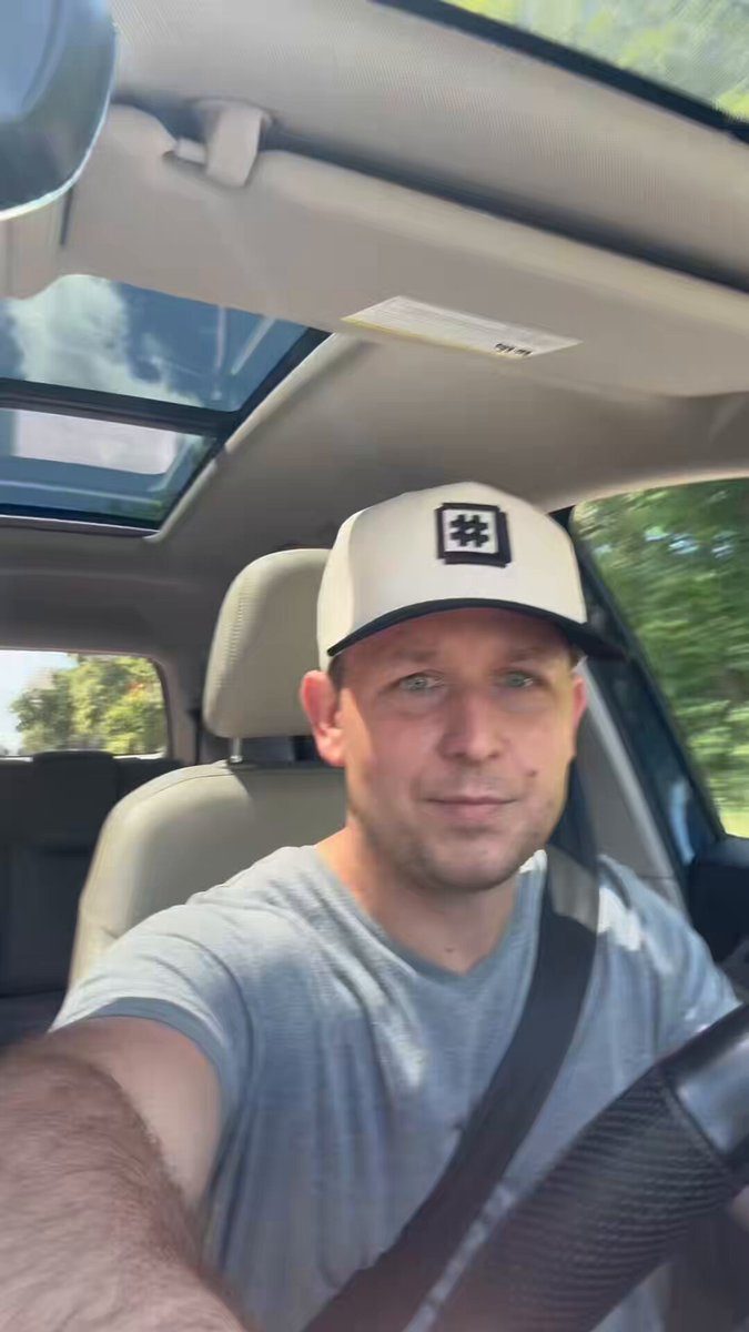 The image features a man wearing a white baseball cap with an "X" on it, sitting inside a car. The man appears to be smiling as he looks directly at the camera. There are also some text elements in the image that read "Blaze on X News - 6.21.26 Posting is hard sometimes DeltaSauce drop this past week Ordinals dotio marketplace drops tomorrow!!!".