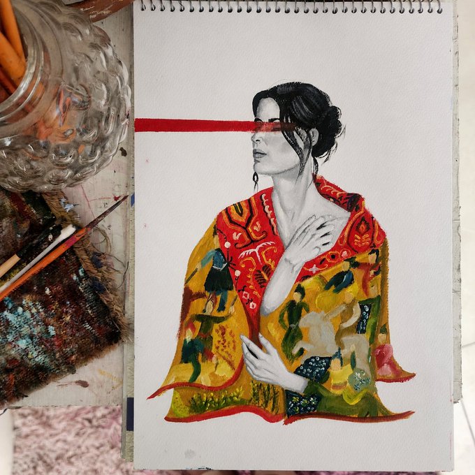An artistic painting in a spiral sketchbook showing a woman in profile with a red blindfold, draped in a vibrantly patterned red, yellow, and green robe, displayed next to paint supplies and brushes.