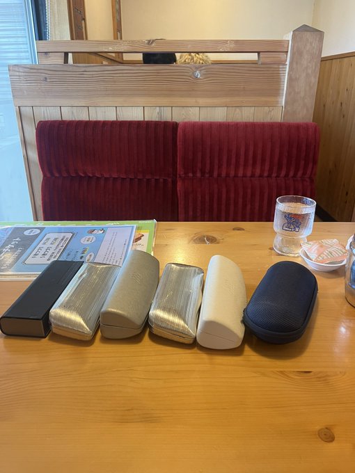 urn of flowers sits on a wooden table, accompanied by six pairs of glasses and a menu at a restaurant.