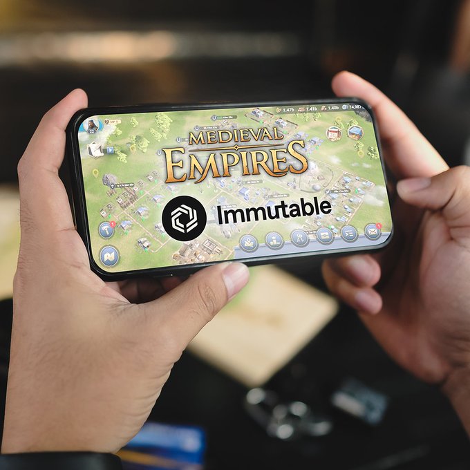 A pair of hands holding a smartphone displaying the mobile game 'Medieval Empires' with the 'Immutable' logo overlaid on the screen.