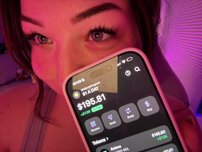 A close-up selfie of a person with pink lighting showing a phone screen displaying a crypto wallet app with $195.81, a 3.75% gain, and Solana (SOL) tokens visible.