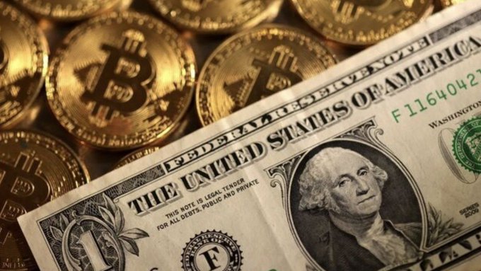 A close-up photograph showing physical Bitcoin tokens stacked together with a United States one-dollar bill placed in the foreground.