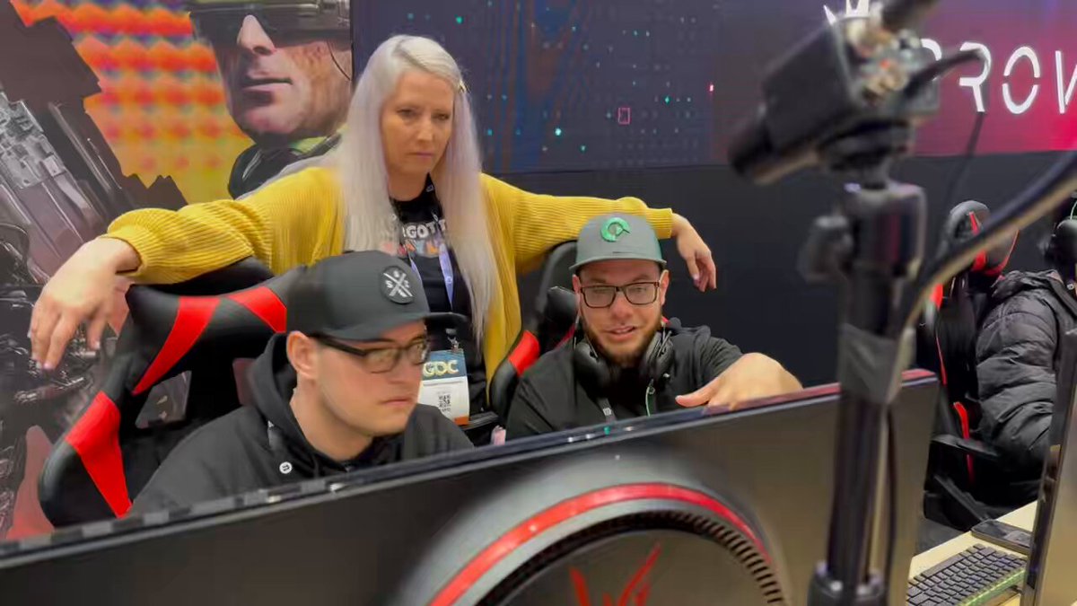 The image shows a group of three people sitting around a computer monitor, likely playing video games together. One person is wearing glasses and has a hat on their head. The other two individuals are also wearing hats. They appear to be enjoying themselves as they engage in an interactive gaming experience.