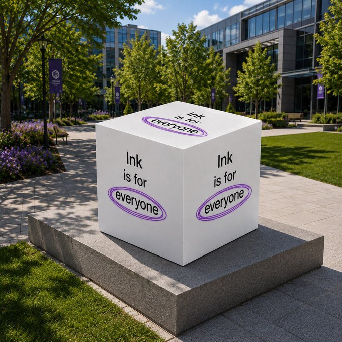 The image features a large white cube sculpture with purple text that reads "ink is for everyone". The sculpture is placed outdoors, surrounded by grass and trees. In the background, there are buildings visible behind the sculpture.