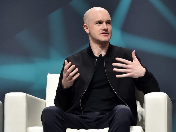 Coinbase CEO Brian Armstrong, a bald man in a black jacket, speaks while gesturing with both hands at what appears to be a conference panel. The image accompanies a post discussing his predictions about crypto regulation, the Clarity Act, and Bitcoin's potential to reach $400,000 by 2030.