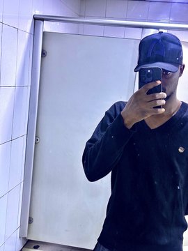 The image features a man wearing a black sweater, taking a selfie with his cell phone in front of a mirror. The man's reflection can be seen clearly as he captures the moment. The background includes white tiles that match the color of the wall behind him. There is also a poster on the wall, which appears to be related to the post about Arc and the upcoming episode of "Builders on Arc".
