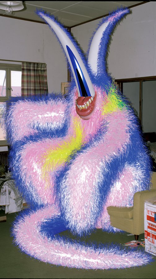 A 3D render of a grotesque pink and blue furry monster with long horns and a wide toothy grin, sitting in what appears to be a Japanese-style room.