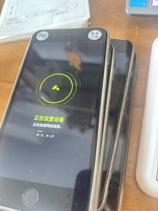 Several smartphones are stacked, with the top one displaying a yellow loading circle and Chinese text indicating a device setup is checking network connection.