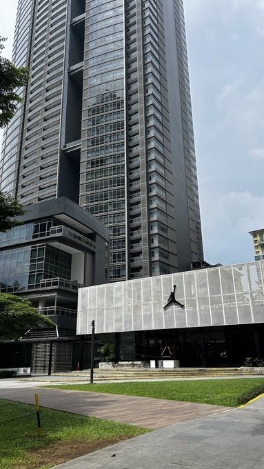 A tall, modern skyscraper with a black facade and a Jordan storefront on the ground level is shown on a cloudy day.
