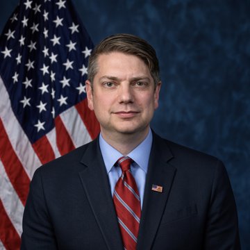The image shows an official portrait of a man in a dark suit and red tie standing in front of an American flag. The accompanying post references legislation related to bitcoin holdings and House Financial Services Committee, suggesting this may be an official photo of a member of that committee involved in advancing the American Reserve Modernization Act.