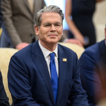 The image features a man wearing a suit, sitting down with his hands resting on his lap. He appears to be looking off into the distance or deep in thought. The text "LATEST: Treasury Secretary Scott Bessent says the US Strategic Bitcoin Reserve is proceeding" suggests that there might have been an important announcement related to cryptocurrency or the economy. The man's attire and posture indicate a formal setting, possibly during a press conference or meeting.