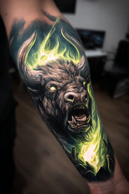 A vibrant tattoo on a person's arm features a snarling bison head surrounded by glowing green flames and dark smoky shading.