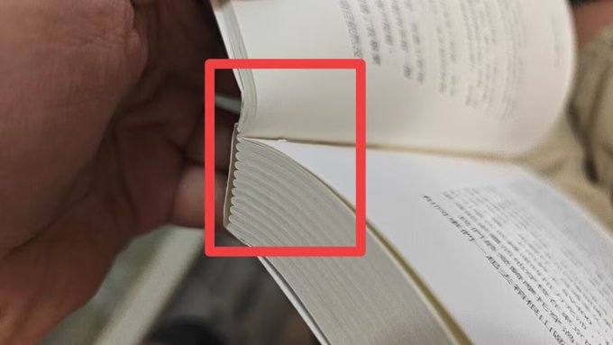 A close-up photo shows a person's hand holding open a book, with a red rectangle highlighting the decorative scalloped edge of the pages.