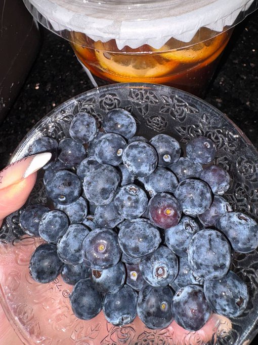 The image features a bowl filled with blueberries placed next to a plastic lid or container. The bowl contains approximately 12 blueberries, which are the main focus of the scene. The background appears to be a kitchen countertop, suggesting that this might have been prepared in a home setting. The post seems to be about food and eating habits, possibly discussing the importance of healthy snacking options like fruits such as blueberries.