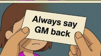 The image features a cartoon girl holding up a piece of paper with text that reads "Always say GM back" written in black marker. The girl appears to be wearing a pink shirt, which stands out against the blue background of the image.