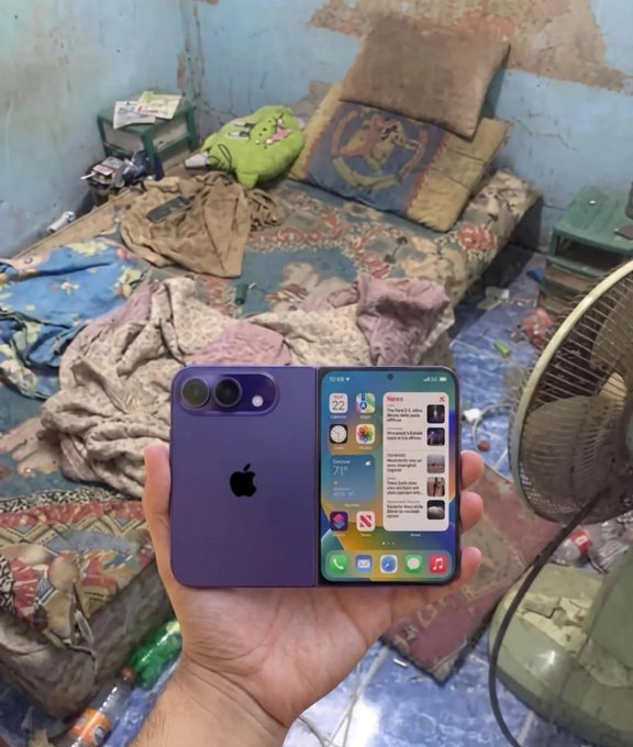 A hand holds up an open purple foldable iPhone displaying its screen, showing the home screen with various apps, set against the backdrop of a cluttered bedroom.