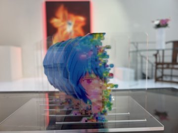 A glitch-style digital art piece of a colorful, dissolving head displayed inside a clear acrylic case in a gallery setting.