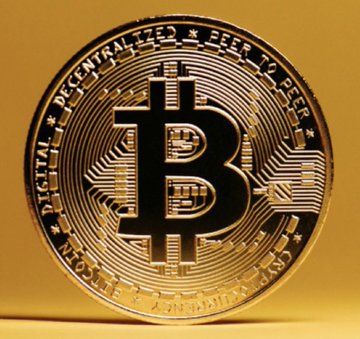 A close-up of a gold-colored physical Bitcoin coin featuring the iconic ₿ symbol and the inscription "DIGITAL DECENTRALIZED PEER TO PEER," visually reinforcing the post's claim that the Kanoo Group, a major UAE family office, has been quietly stockpiling BTC alongside its traditional investments in real estate, shipping, and oil.