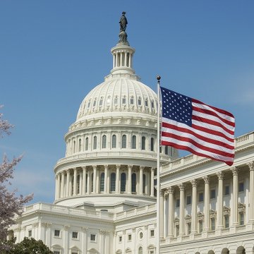 The U.S. Capitol Building's iconic dome and the Statue of Freedom stand against a clear blue sky, with an American flag waving prominently in the foreground, symbolizing political activity. The image relates to the post by suggesting a busy week of congressional or governmental events ahead in Washington, D.C.