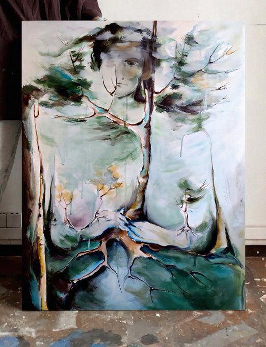An abstract mixed-media painting on canvas featuring a face emerging from a forest scene with green, teal, and earthy tones, leaning against a wall on a paint-splattered floor.