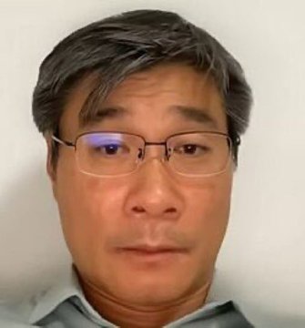 A close-up portrait shows an older man with short graying hair wearing glasses and a gray polo shirt.