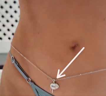 A close-up image shows a thin silver chain waist accessory with keys and a lock charm pendant resting against bare skin, with a white arrow pointing to the pendant. The post asks Grok to identify the name and price of the chain Kylie Jenner is wearing around her waist, which the image displays up close.