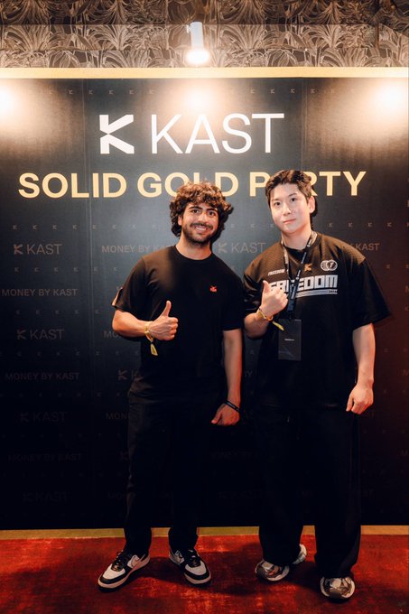 Two young men pose smiling and giving thumbs up in front of a black backdrop displaying 'K KAST MONEY BY KAST' and 'SOLID GOLD PARTY' at an event.