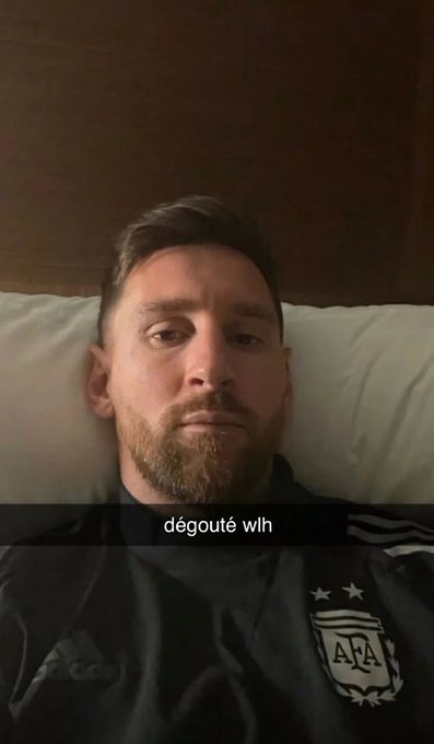 A close-up photo of Lionel Messi lying in bed wearing an Argentina national team training top, with a Snapchat-style caption 'dégoûté wlh' overlaid.