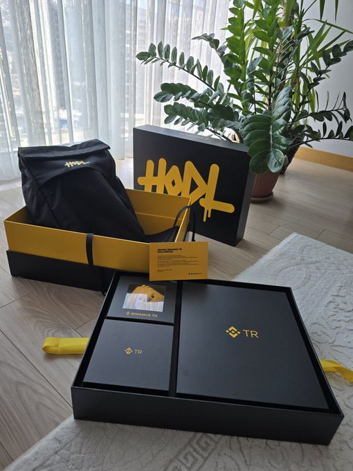A black Binance TR package set is displayed on a wooden floor, featuring a backpack, branded boxes marked with "HODL" graffiti art and "TR" logos, alongside a small Binance TR info card, thanking the Binance TR team for the thoughtfully prepared gift.