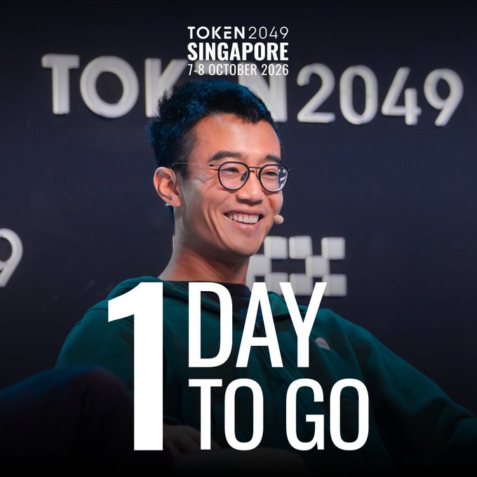 A smiling man with glasses and a headset microphone stands before a "TOKEN 2049" backdrop, with the overlay text "1 DAY TO GO" and "TOKEN 2049 SINGAPORE 7-8 OCTOBER 2026" promoting tomorrow's final day at Marina Bay Sands.