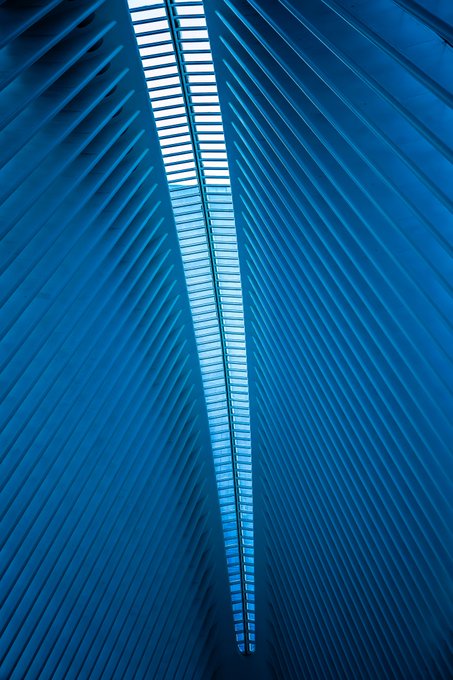 An abstract blue architectural image showing converging diagonal lines that create a pointed, reflective, tunnel-like structure.