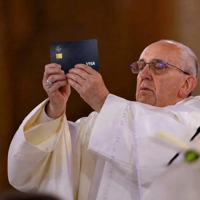 Pope Francis, wearing white vestments and glasses, holds up a dark blue Visa card with a chip.