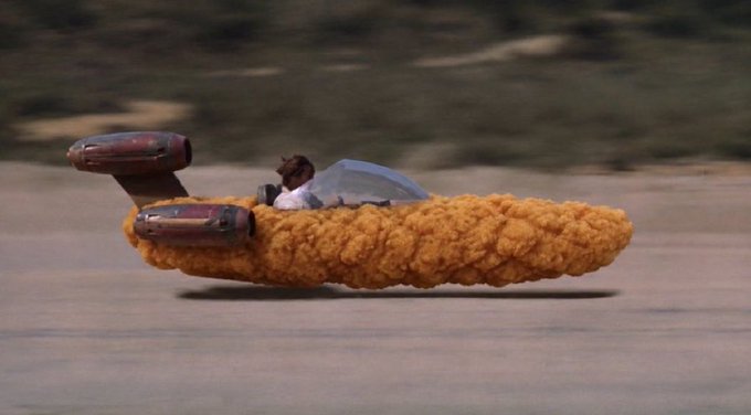 A futuristic hover-speeder shaped like a breaded chicken nugget soars across a desert landscape, piloted by a figure in a cockpit. The absurd "nugget ship" image satirizes the post's longing for a perfect "cult coin," joking that such an ideal crypto asset is just as fantastical as a giant fried chicken nugget floating through the air.
