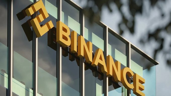 The yellow Binance logo is prominently displayed on the exterior of a modern glass building.