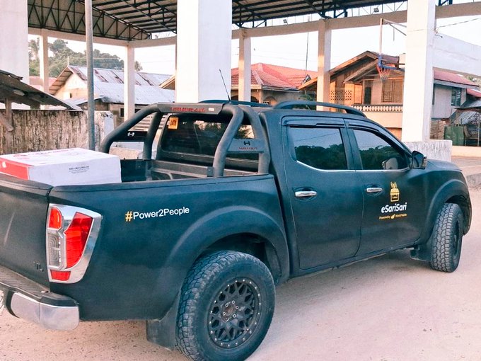A black pickup truck parked under a metal structure, featuring the 'eSariSari' logo, '#Power2People' text, and a white box in the truck bed.