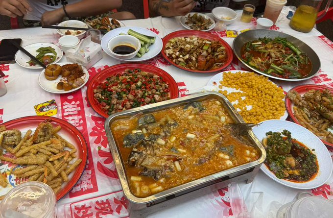 A table laden with various Chinese dishes including crab, stir-fried meat with peppers, corn, fish in spicy broth, and other banquet foods.
